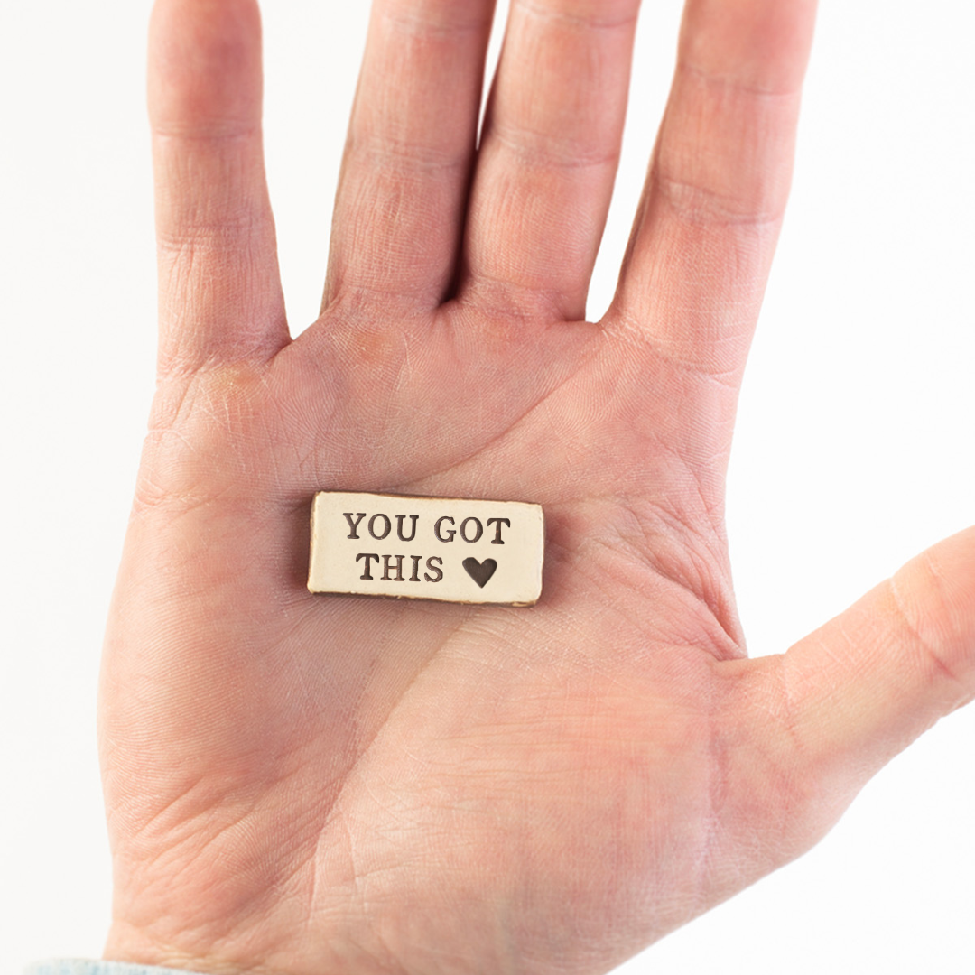 Hand holding a small pocket rock that reads &