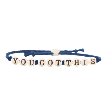 The Joni x MudLOVE Friendship Bracelet 4-Piece Set displaying a blue cord bracelet with beads spelling &